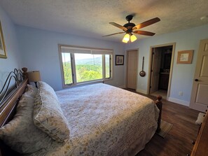 Ein Schlafzimmer mit einem Bett, einem Deckenventilator, einem Fenster mit Aussicht und einer Tür zu einem anderen Raum.