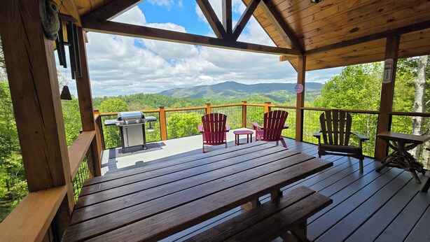 Um deck de madeira com churrasqueira, cadeiras Adirondack e uma mesa.