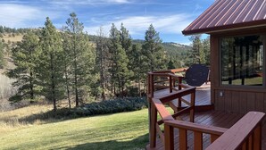 A wooden deck with a metal roof overlooking a forested hillside.