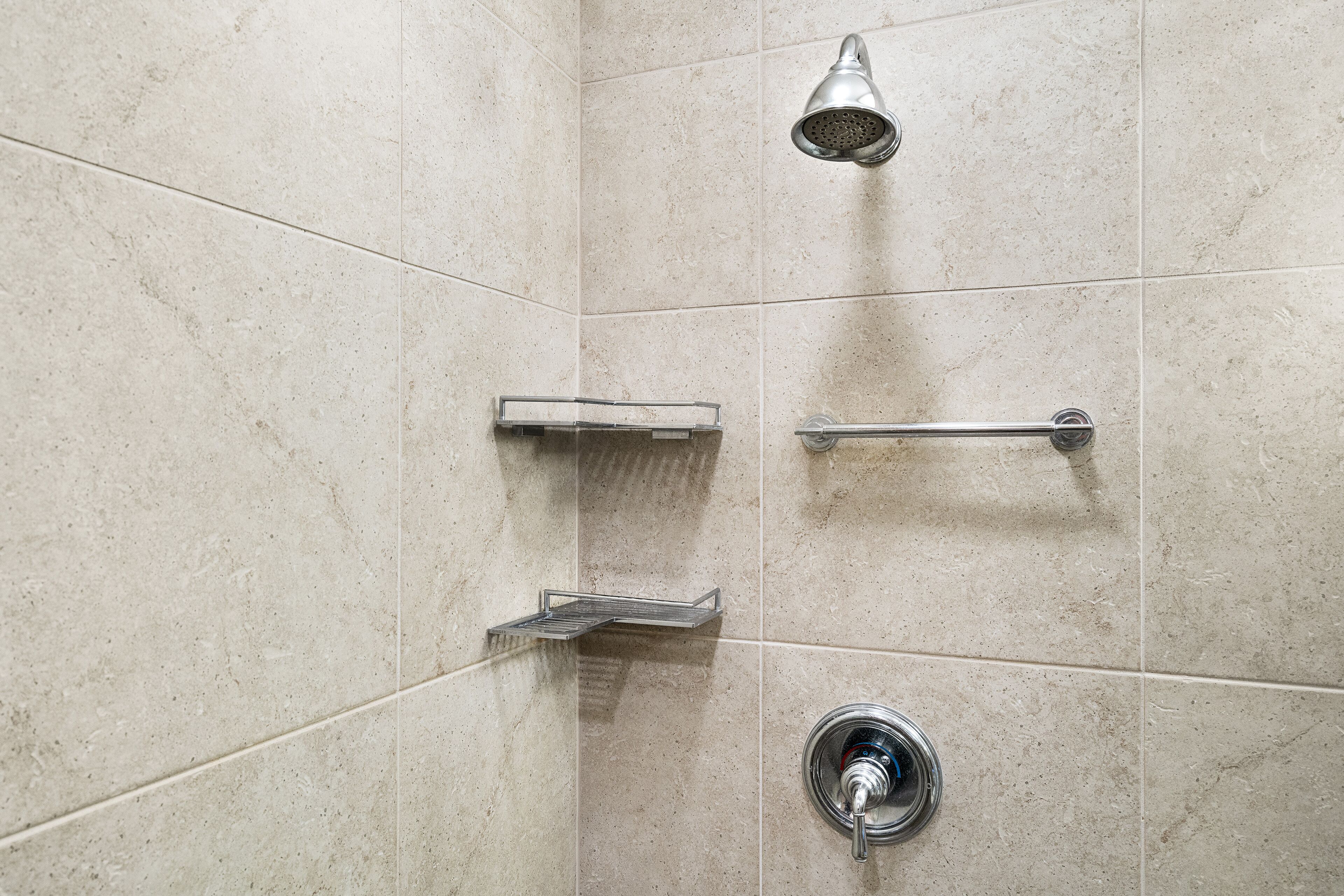 A shower area with a handheld showerhead, a wall-mounted faucet, and a shelf.