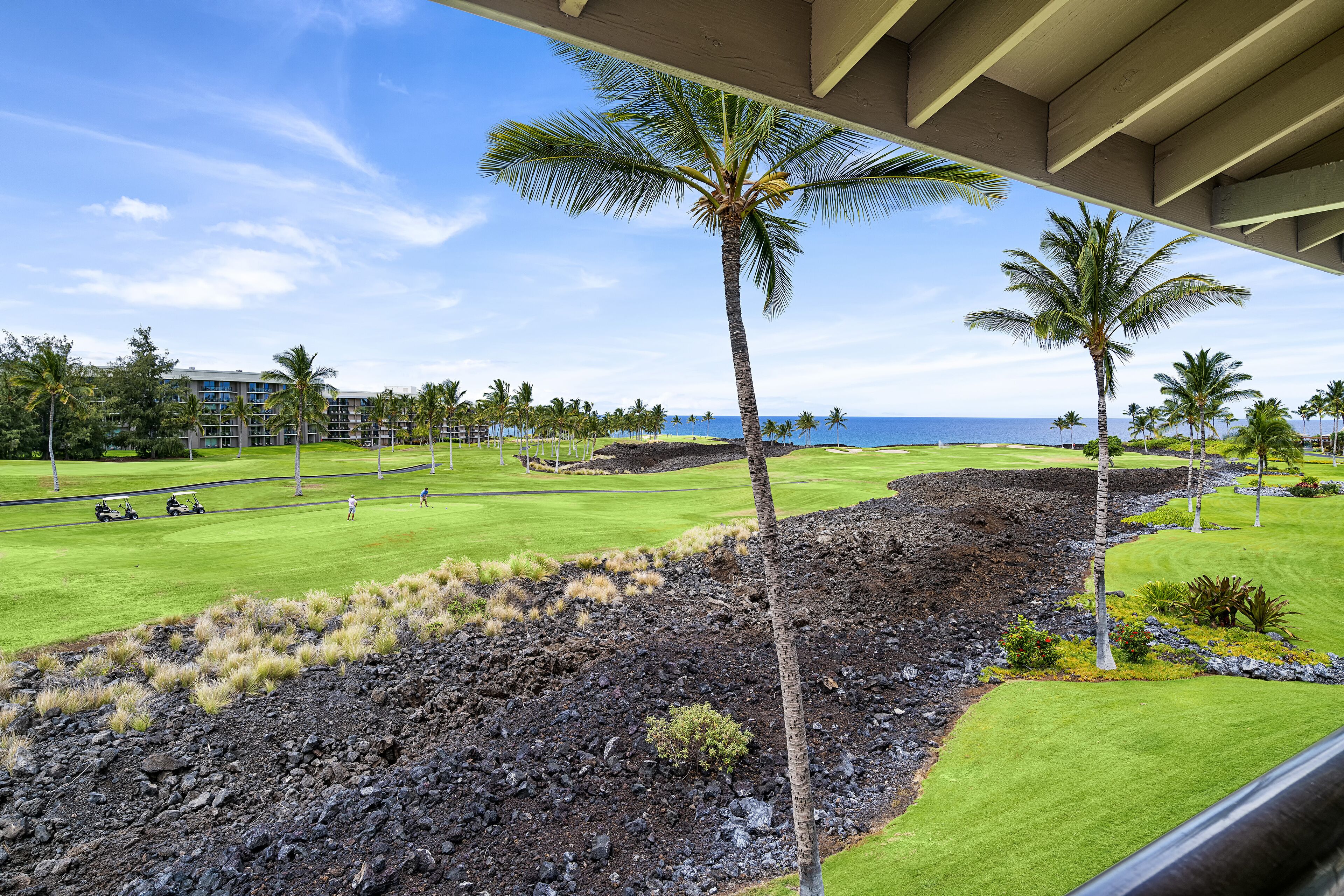 A golf course with a view of the ocean, palm trees, and a building in the background.