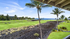 Ein Golfplatz mit Blick auf das Meer, Palmen und ein Gebäude im Hintergrund.