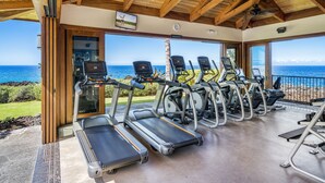 Ein Fitnessraum mit Laufbändern und Trainingsgeräten, großen Fenstern mit Meerblick und einer Holzbalkendecke.
