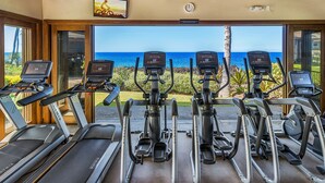 Ein Fitnessraum mit Laufbändern und Crosstrainern, mit Blick auf eine malerische Meereslandschaft.