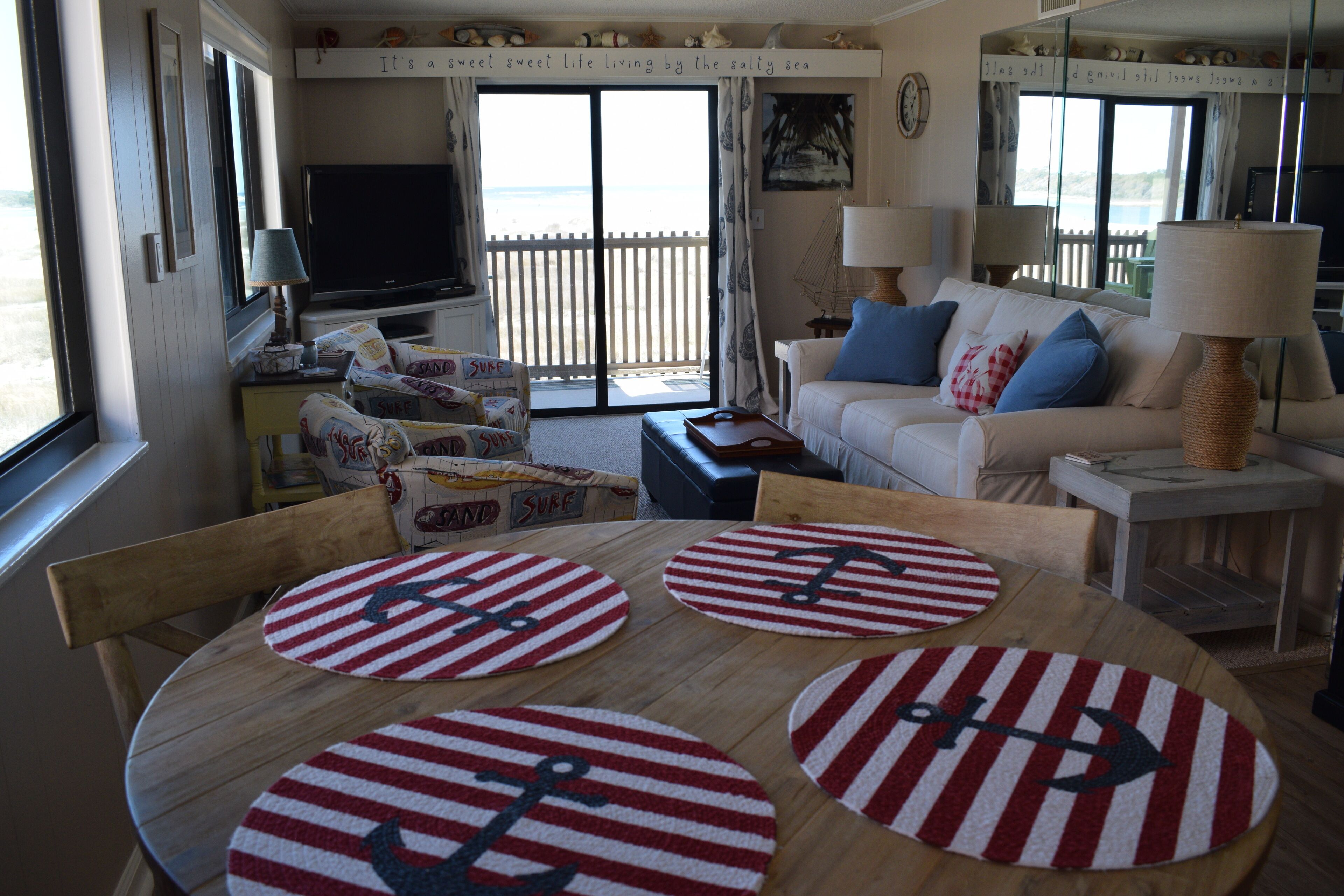 A cozy living room with a large window, a television, a sofa, and a coffee table with striped placemats.