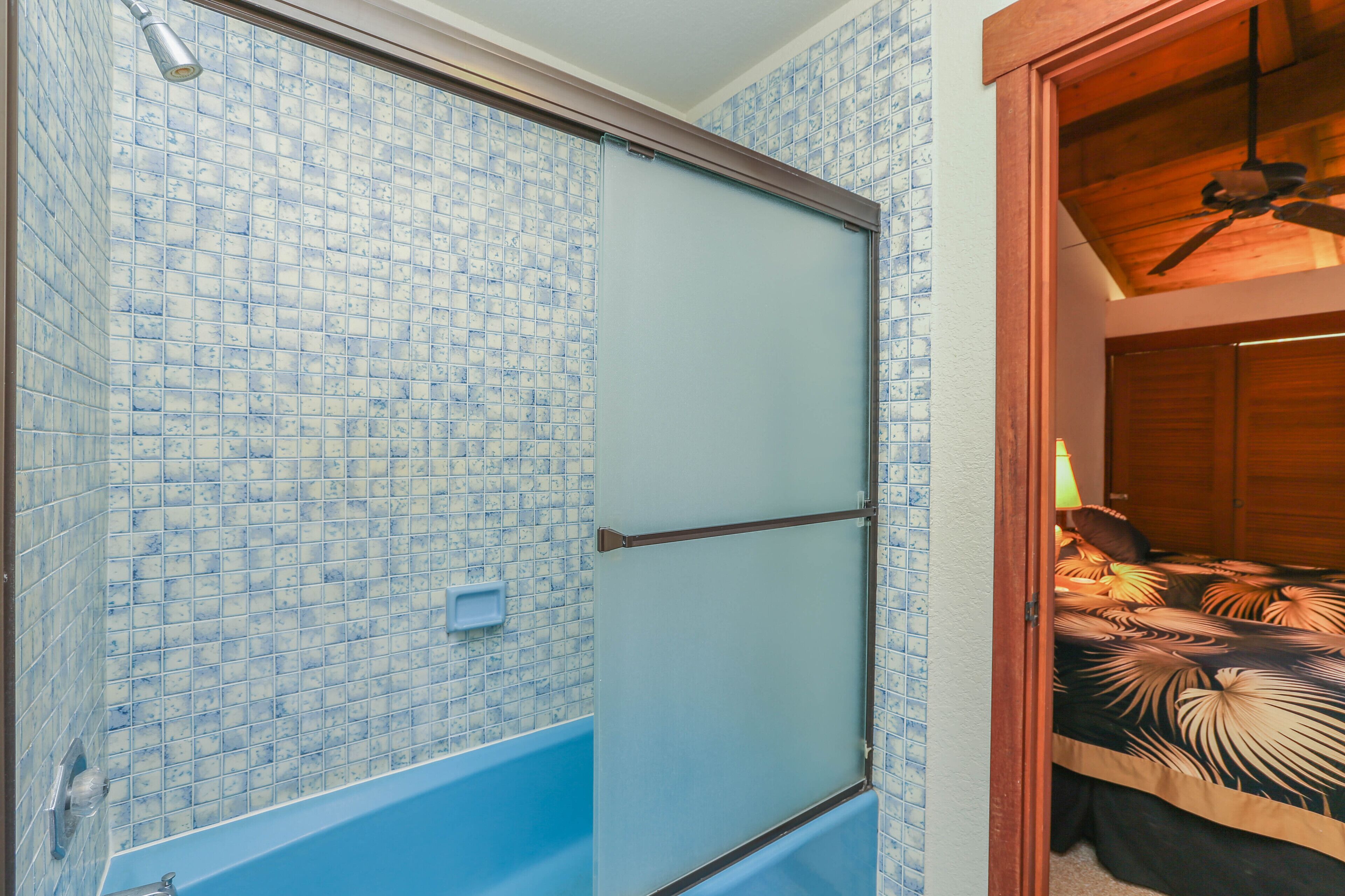 Een badkamer met een blauw betegelde douchecabine, een bad en een houten plafondventilator.
