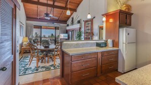 Cozinha com armários de madeira, geladeira e área de refeições com cadeiras e mesa.