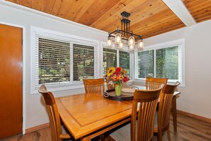 A dining room with a wooden table and chairs, a chandelier, and a window with blinds.