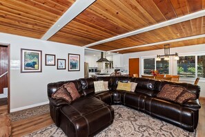 A spacious living room with a large leather sectional sofa, wooden ceiling beams, and framed pictures on the wall.