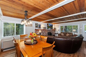 A spacious living area with a wooden ceiling, a dining table with chairs, a brown leather sofa, and a fireplace.