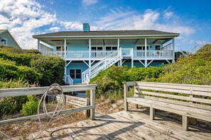 A two-story beachfront house with a balcony and stairs leading to the upper level.