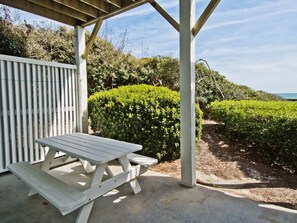 A covered picnic table with benches, surrounded by greenery and a view of the sea.