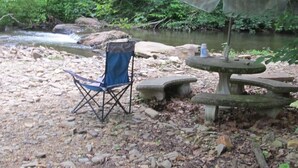 Une chaise et une table en pierre près d’un ruisseau, dans une zone boisée.