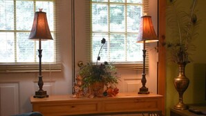 Une pièce avec un bureau en bois, deux lampes, un vase contenant des fleurs séchées et une chaise.