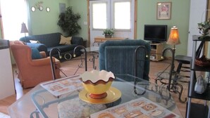 Un salon avec une table basse en verre, un canapé, un fauteuil, un téléviseur et une lampe.