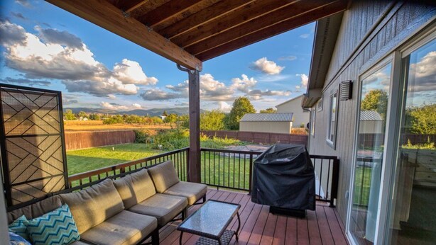 A covered deck with a sofa, table, and grill. - Beautiful Spokane Valley Home (Spokane Valley)