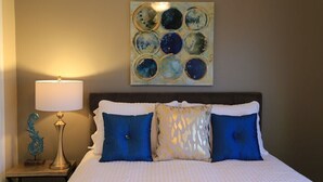 A neatly made bed with blue and white bedding, a wall-mounted abstract art piece, a bedside lamp, and a decorative metal piece on the nightstand. - Beautiful Spokane Valley Home (Spokane Valley)