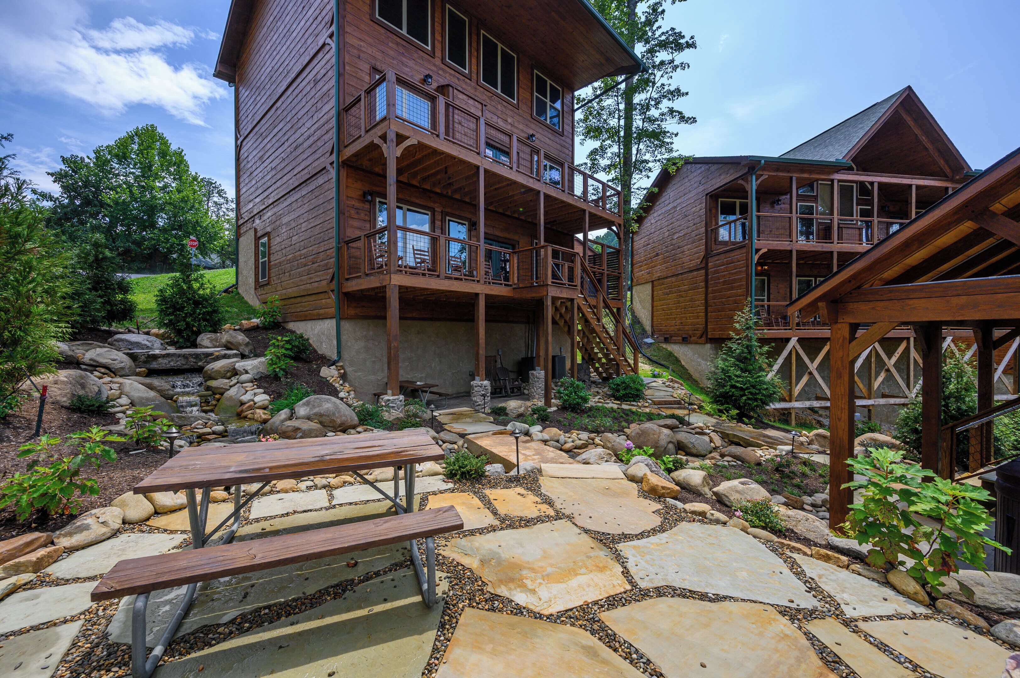 A multi-level wooden cabin with outdoor seating and a stone patio.