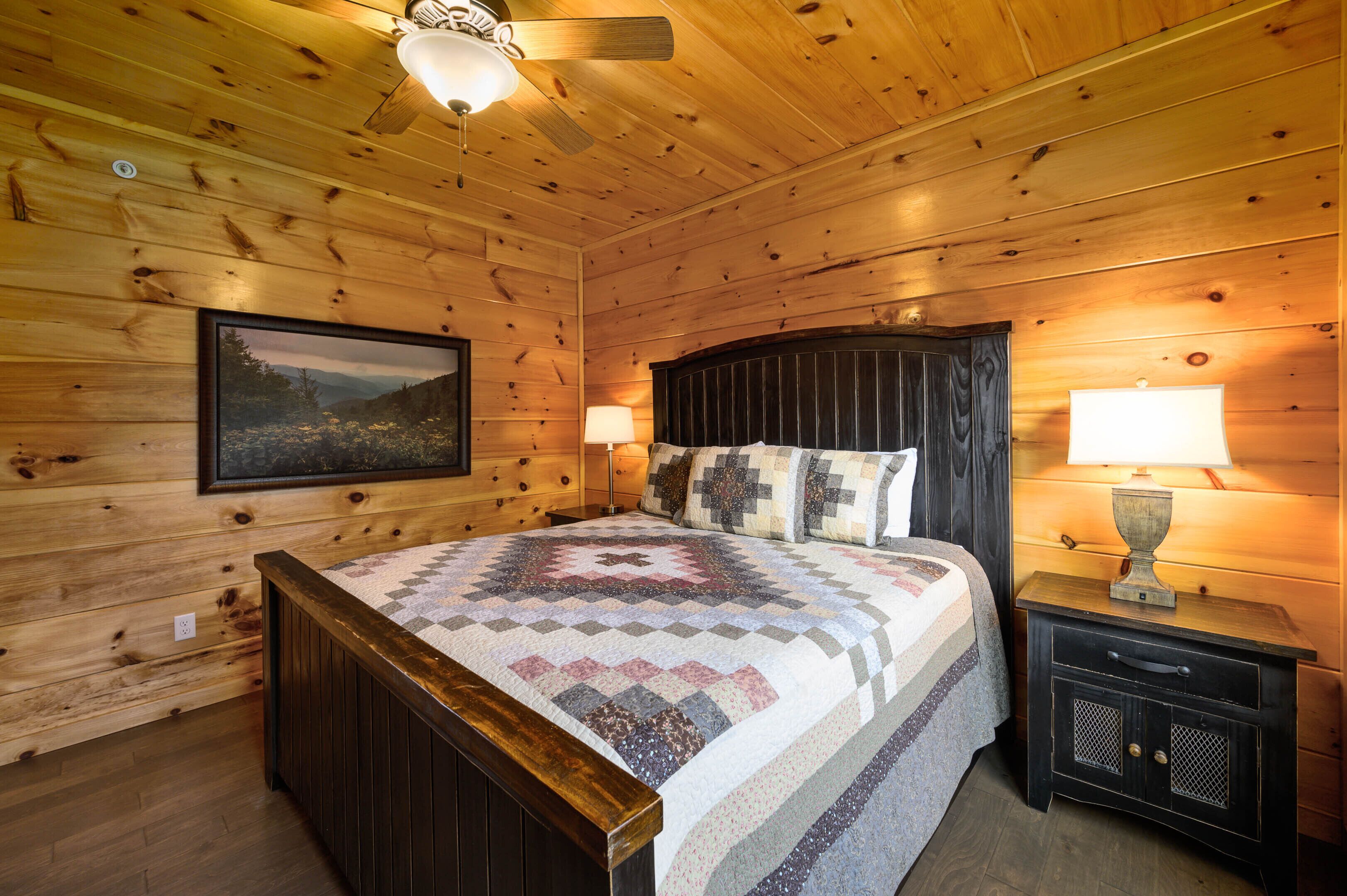 A wooden-paneled bedroom with a bed, two bedside lamps, a nightstand, and a framed picture on the wall.