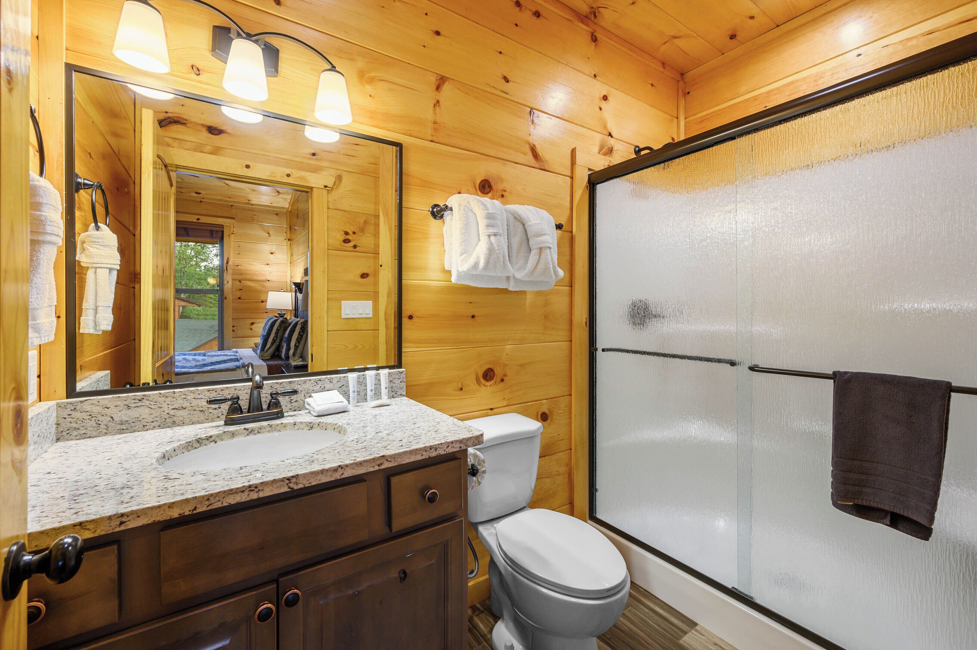 Un baño de cabaña de madera con lavamanos de granito, inodoro y mampara de cristal.