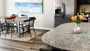 Una cocina moderna con un refrigerador de acero inoxidable, una mesa de comedor con sillas y una mesa redonda con un florero.