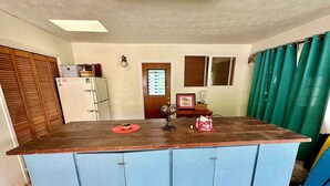 A kitchen with a central island, a refrigerator, a wooden door, and a window with blinds. - SURFERS DREAM STUDIO (Waianae)