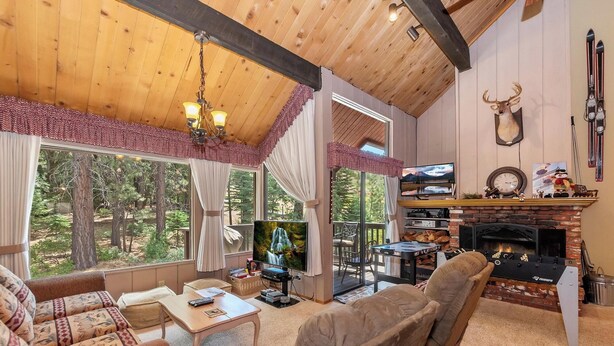 A cozy living room with a fireplace, a television, and a large window overlooking a forest. - Walk to Snow Summit! National Forest & Ski Slope Views! Close to Hiking Trails! (Big Bear Lake)