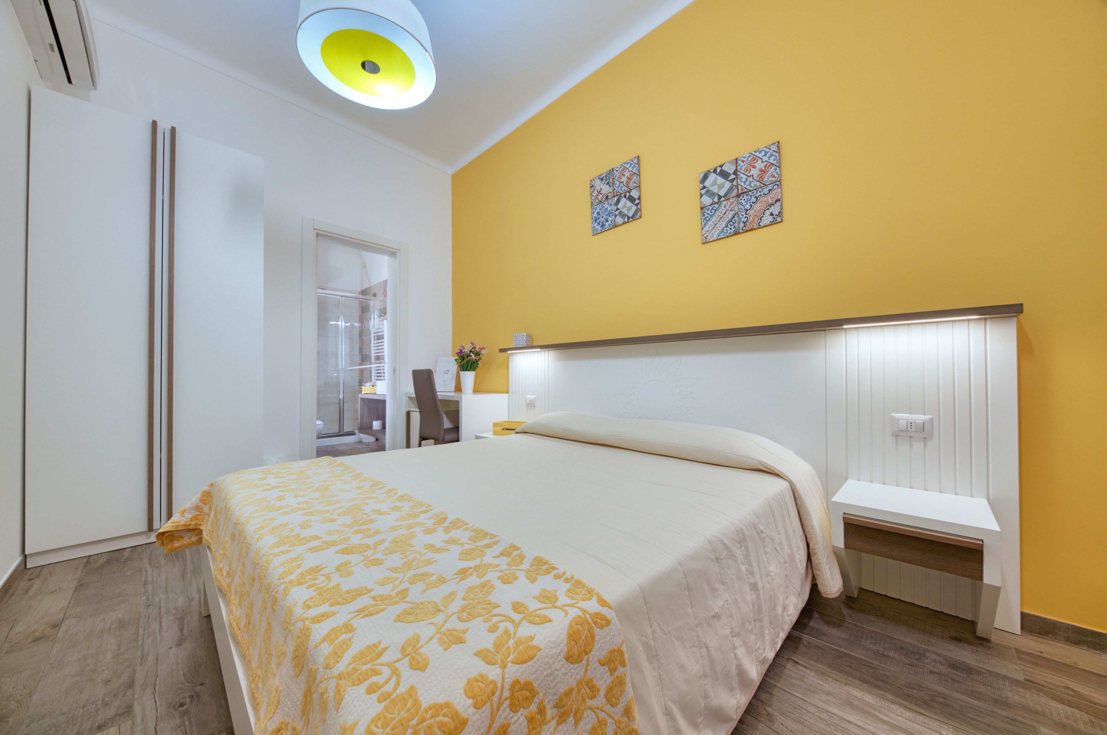 A bedroom with a bed, a bedside table, a nightstand, a desk, and a chair.