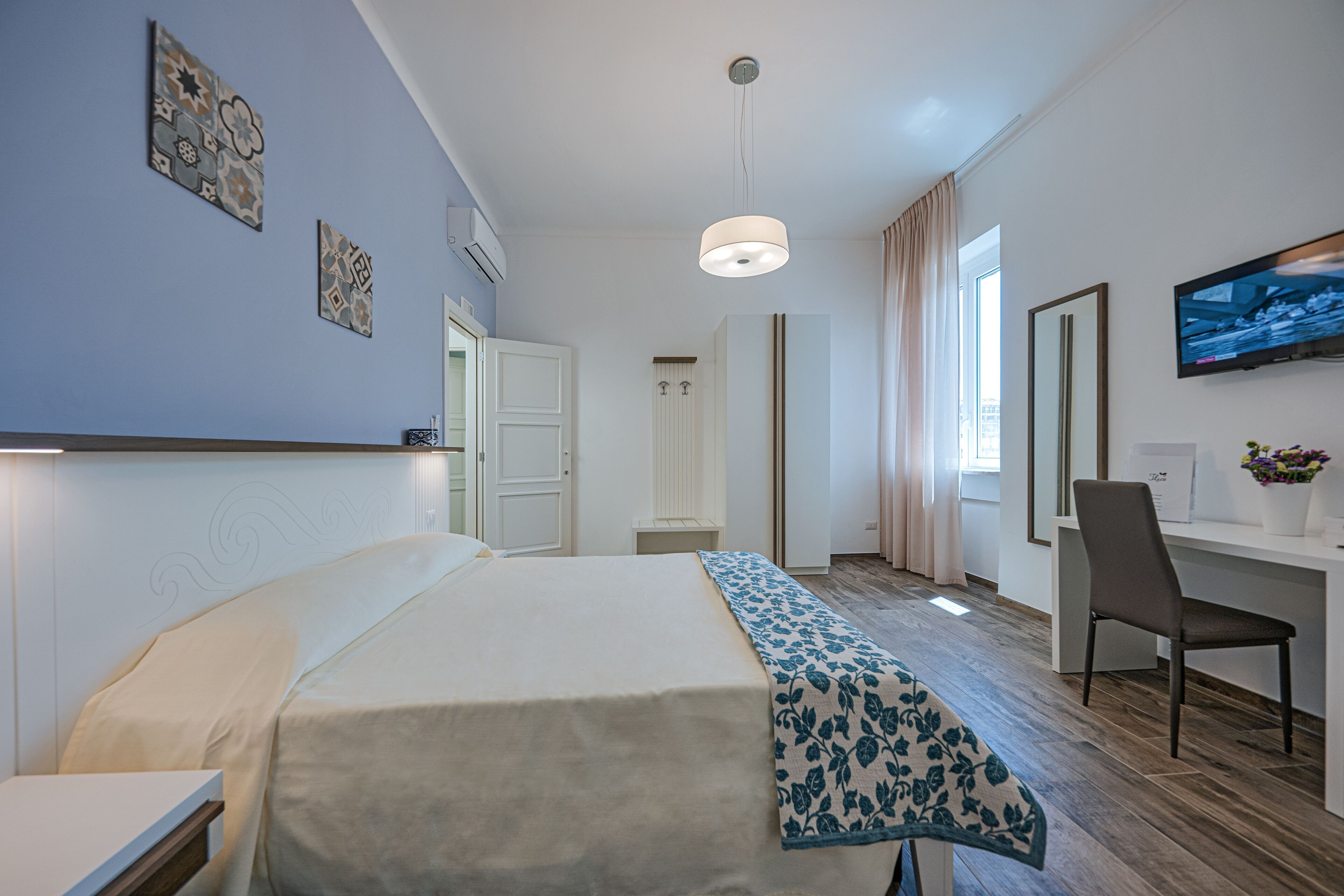 Une chambre d’hôtel avec un lit, un bureau, une chaise, une télévision et une fenêtre avec des rideaux.