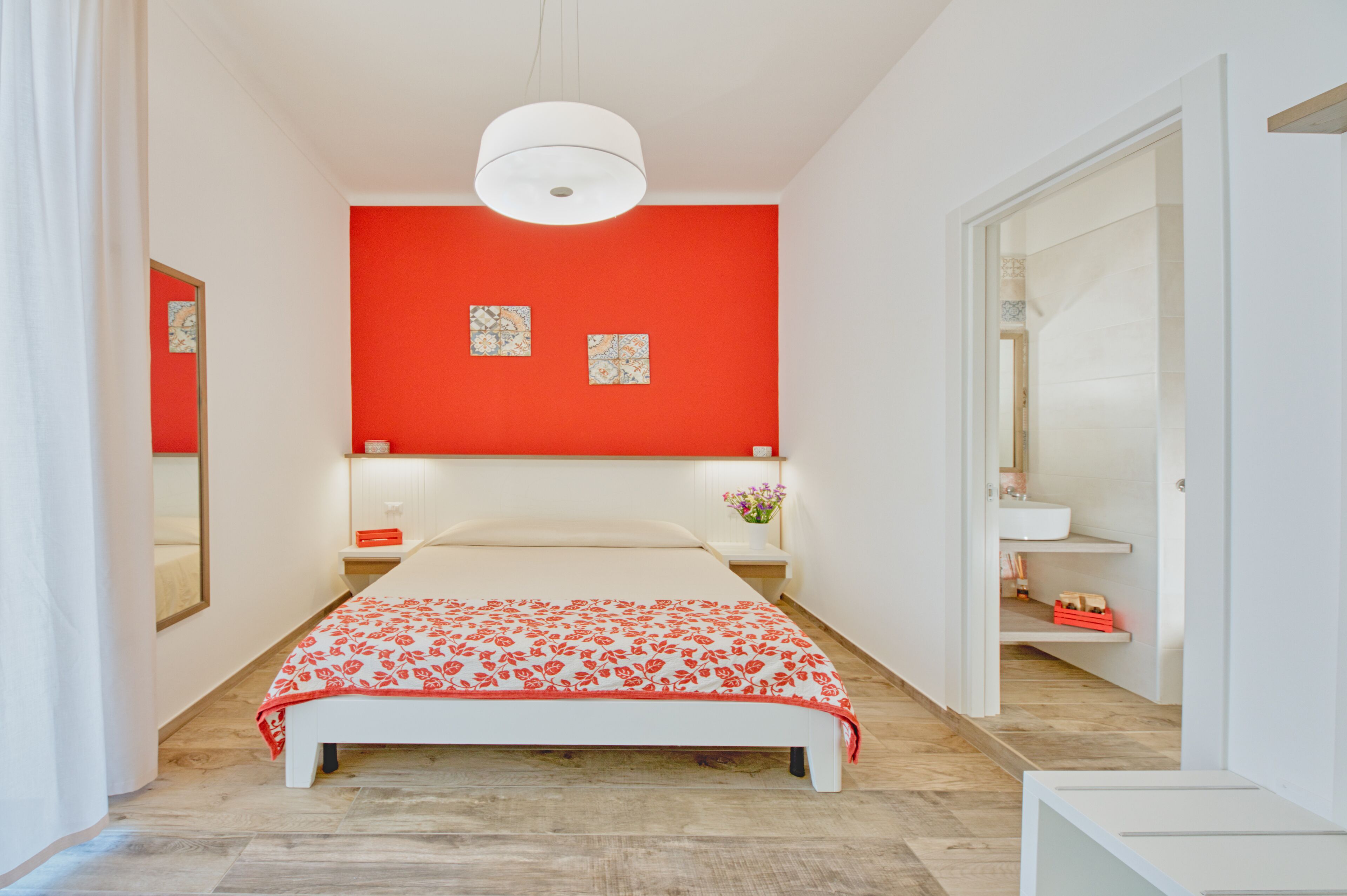 Une chambre à coucher avec un lit, un mur d’accent rouge, un luminaire blanc au plafond et un plancher en bois.