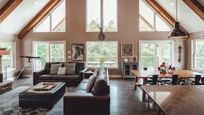 A spacious living area with a high ceiling, large windows, a wooden dining table, and a cozy seating arrangement. - Chieftain Meadows 20+ private acres, Hot Tub, Trails, FirePit, Wifi, Game Room (Rockbridge)