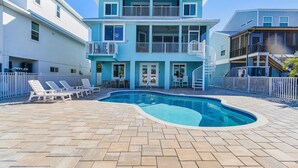 Una casa de dos pisos con piscina, mobiliario exterior y un patio cercado.