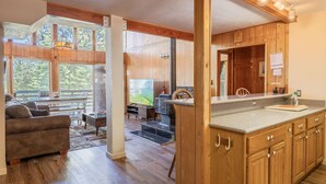 A spacious living area with a large window, wooden flooring, a sofa, and a fireplace. - Cub's cabin Family house inside the gates of Yosemite Park!!! (Yosemite National Park)