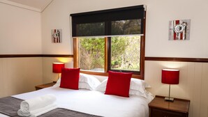 A neatly made bed with white linens and red pillows, a bedside table with a lamp, and a window with a view of greenery. - 2 Bedroom Chalet offers 2 separate bedrooms with a large living/dining area and balcony. (Margaret River)