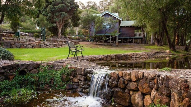 A rustic cabin with a stone waterfall, surrounded by lush greenery and a small wooden deck. - 2 Bedroom Chalet offers 2 separate bedrooms with a large living/dining area and balcony. (Margaret River)