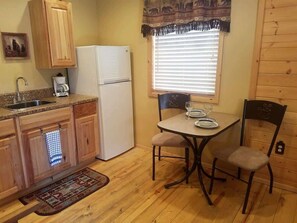 A compact kitchen with wooden cabinets, a refrigerator, a coffee maker, and a dining table with two chairs.