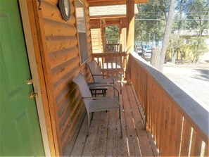 A wooden deck with metal chairs and a table, a green door, and a view of the street.