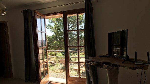 Een kamer met een grote schuifdeur die uitkomt op een buitenruimte met een houten terras en groen.