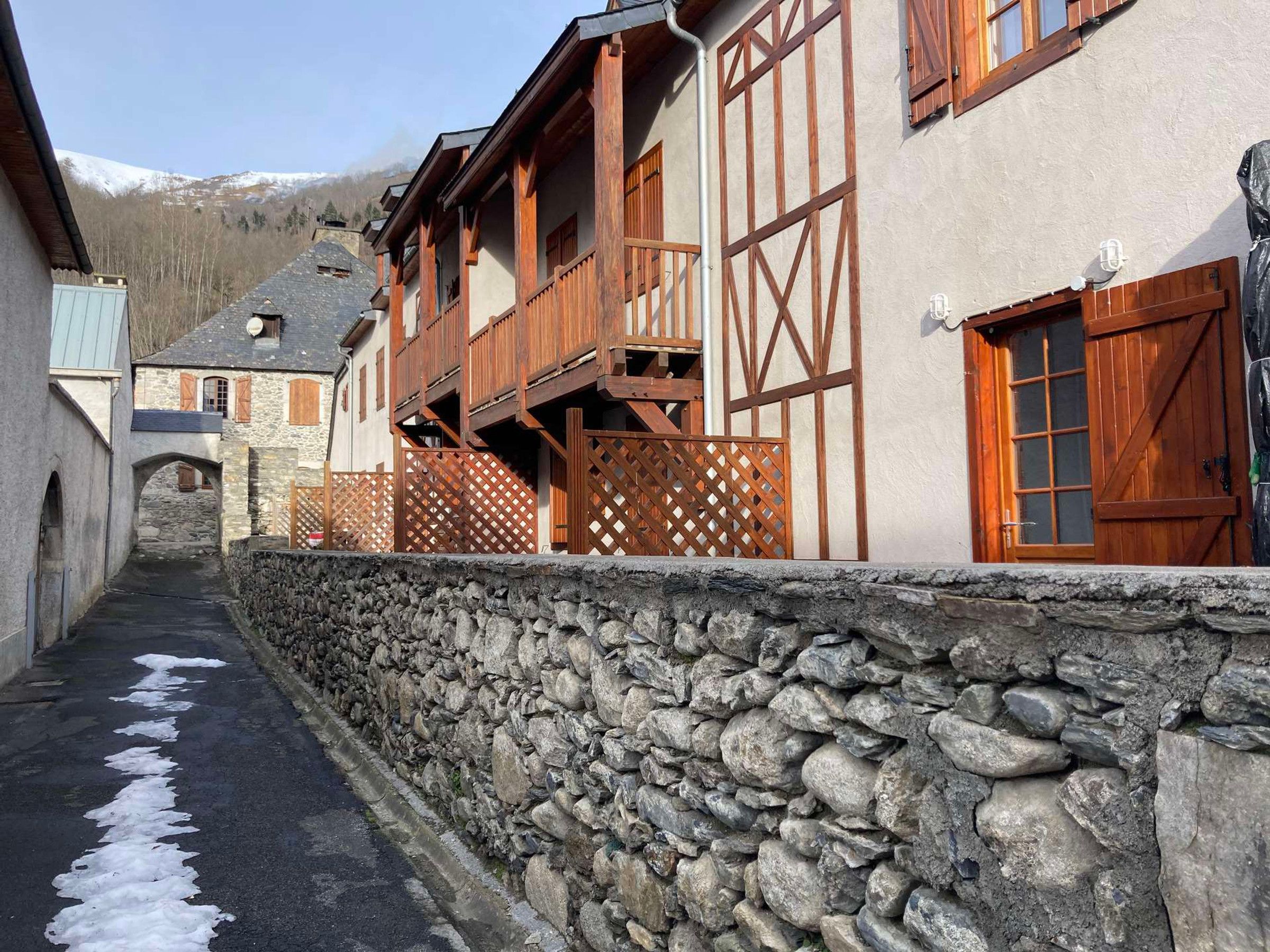 Una calle estrecha con paredes de piedra y edificios de madera, con balcones y un arco de piedra.