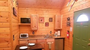 Une cuisine compacte aux murs en bois, équipée d’un four à micro-ondes, d’un grille-pain, d’un évier et d’une porte verte.