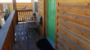 Une cabane en bois avec une porte verte, une terrasse avec des chaises et une fenêtre.