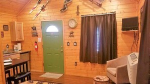 L’intérieur d’un chalet en bois, avec une porte verte, un coin repas, un canapé, un téléviseur et une cheminée.