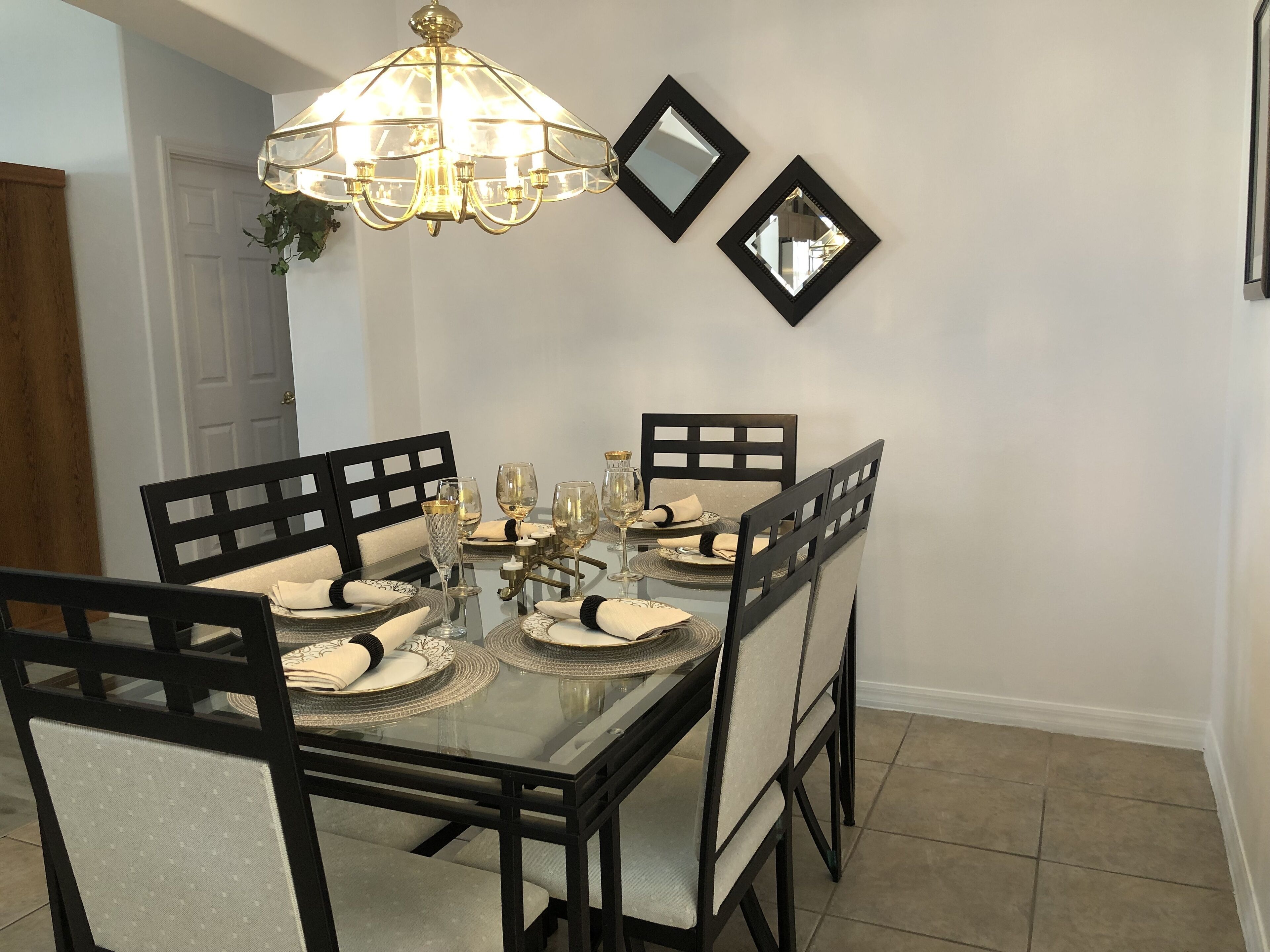 A dining area with a glass table, black chairs, and a chandelier.