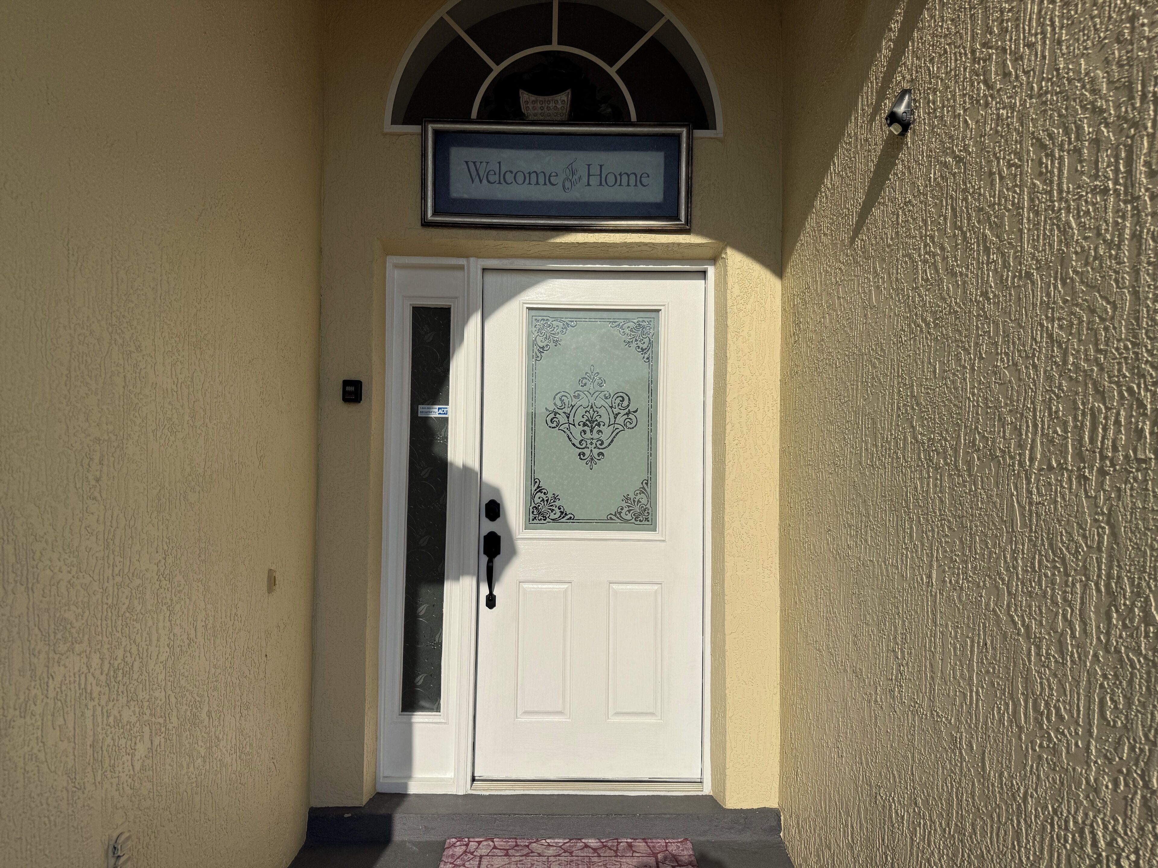 A white door with a decorative glass panel and a 'Welcome To Home' sign above it.