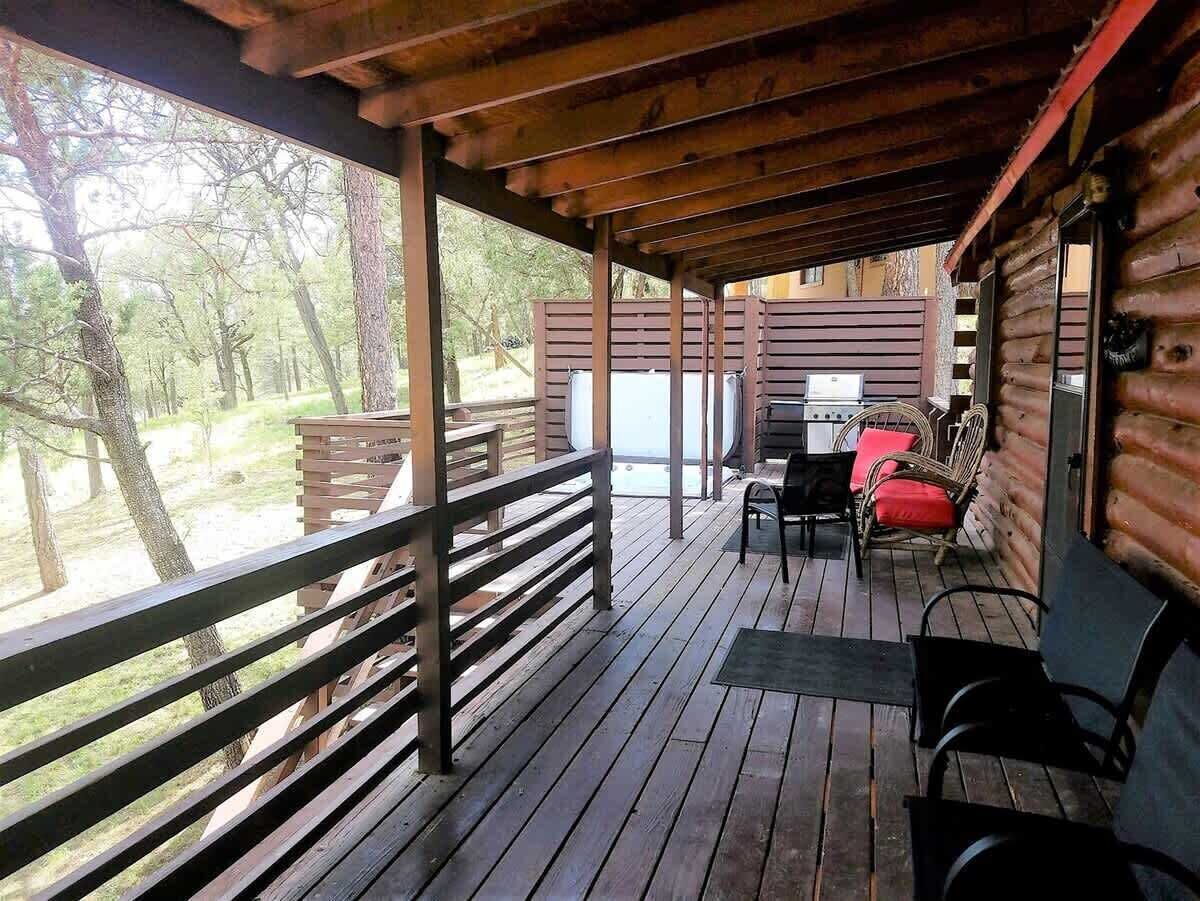 A wooden deck with a railing, a table with chairs, and a view of the surrounding forest.