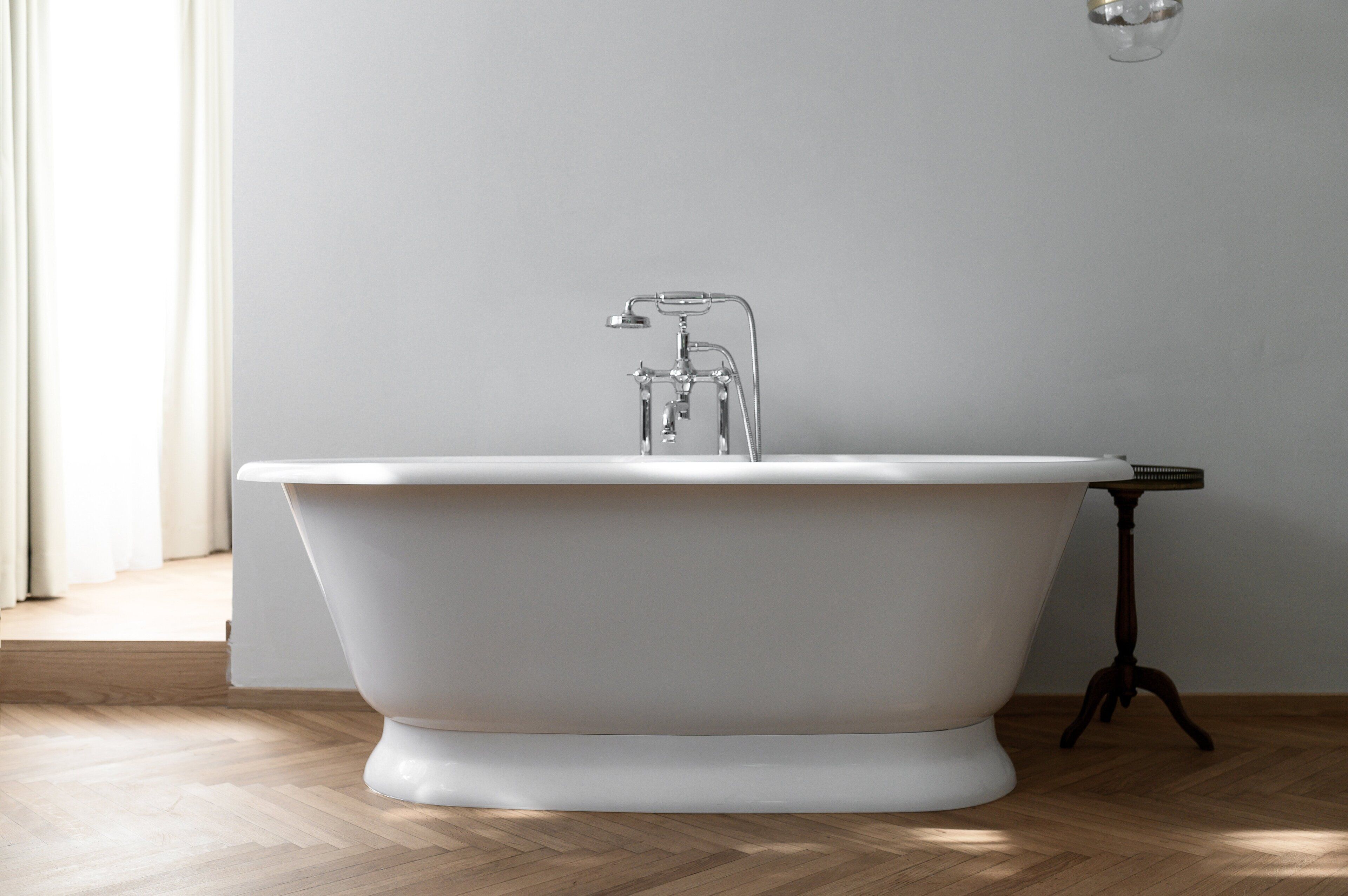 A freestanding bathtub in a bathroom with a wooden floor and a plain wall.