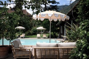 A poolside area with wicker lounge chairs and striped umbrellas. - Villa Arnica (Lana)
