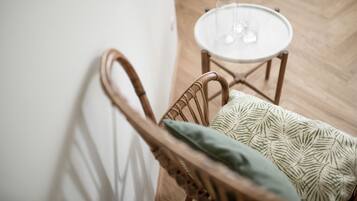 A wicker chair with a patterned cushion and a small round table with a clear glass bottle and glasses.