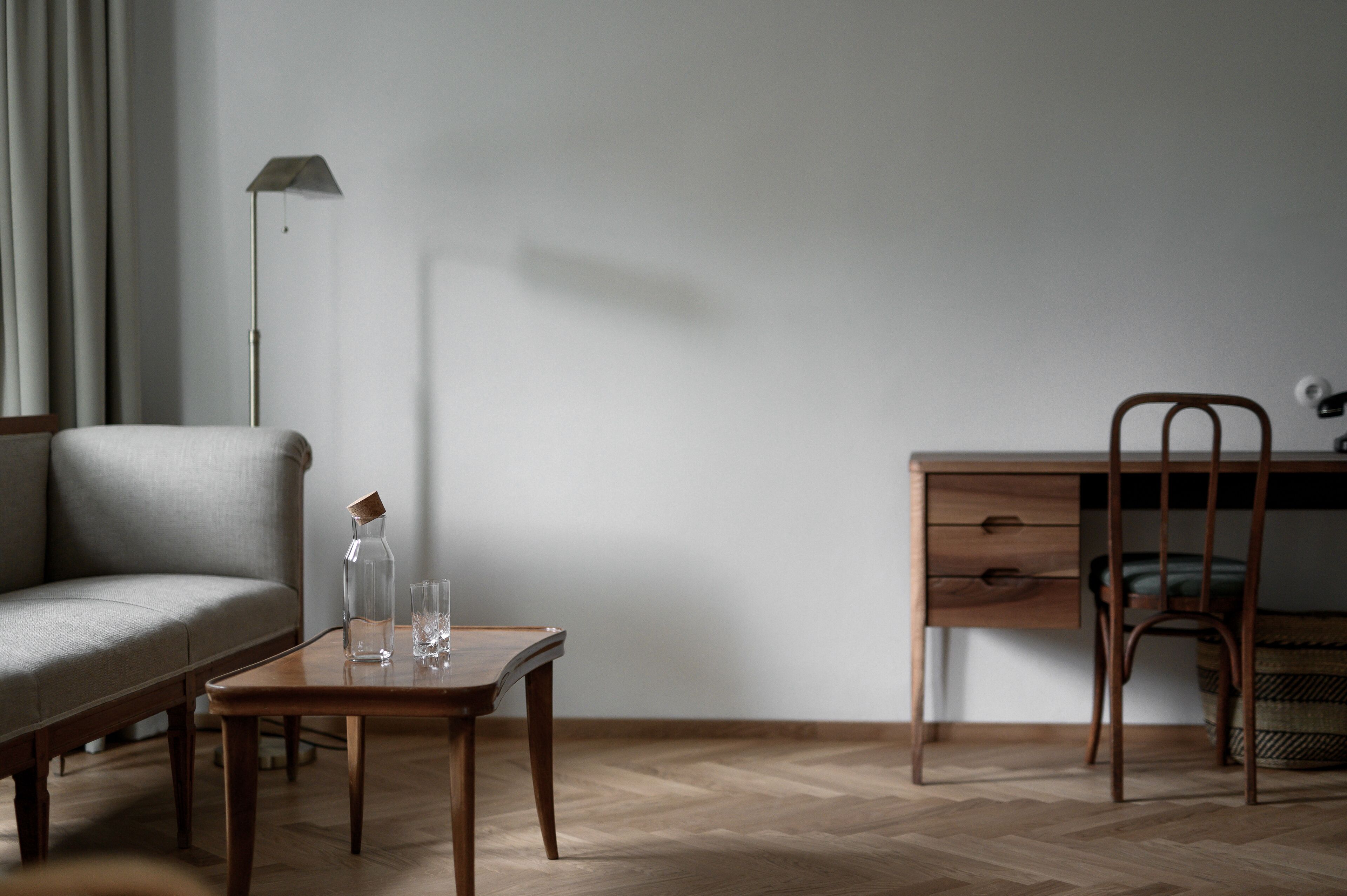 Une pièce au décor minimaliste, avec un bureau en bois, une chaise, un canapé et une petite table sur laquelle se trouvent une bouteille et des verres.