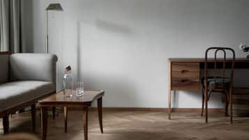 Une pièce au décor minimaliste, avec un bureau en bois, une chaise, un canapé et une petite table sur laquelle se trouvent une bouteille et des verres.